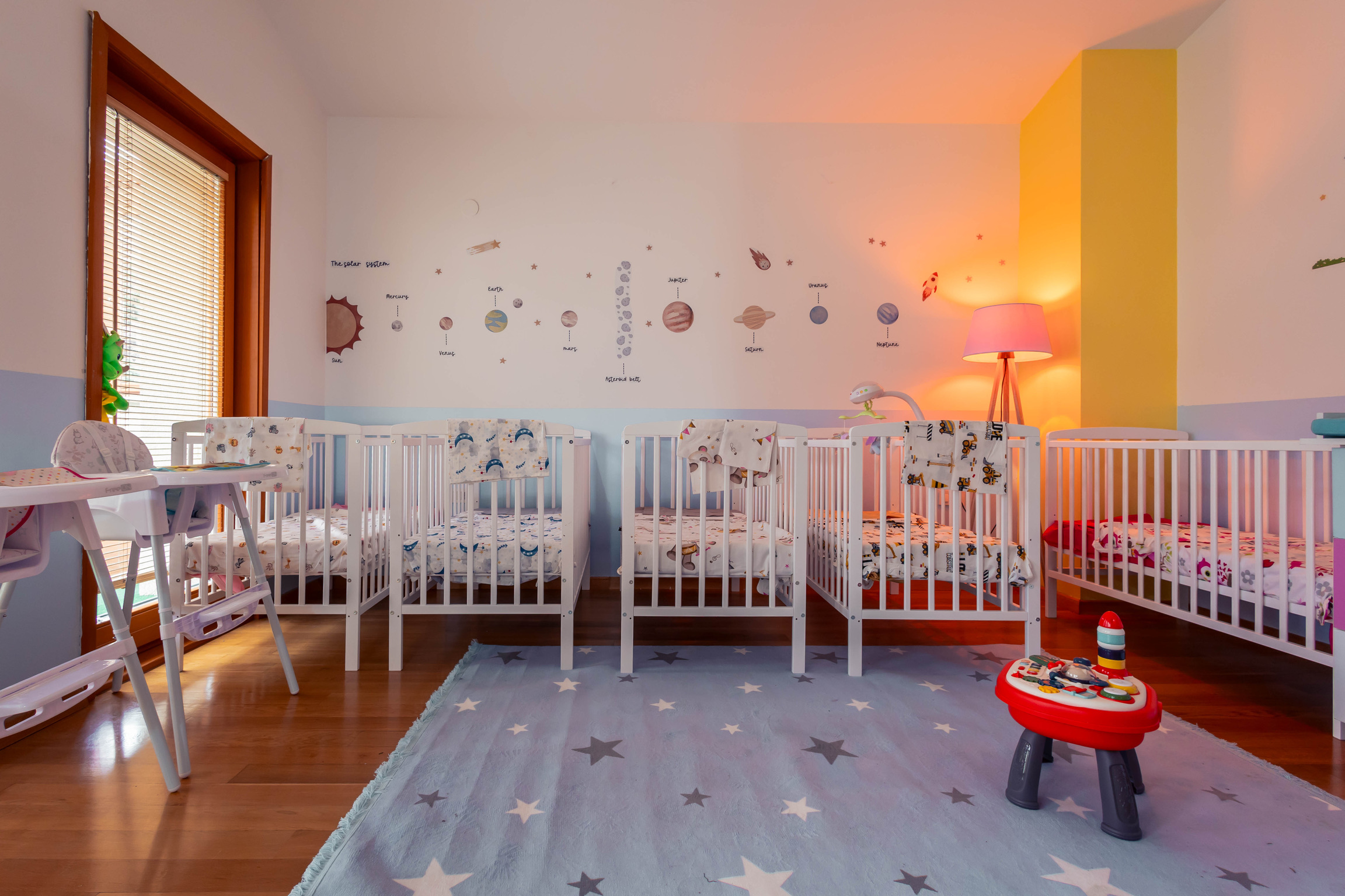 Cozy nursery with cribs and a warm space-themed wall