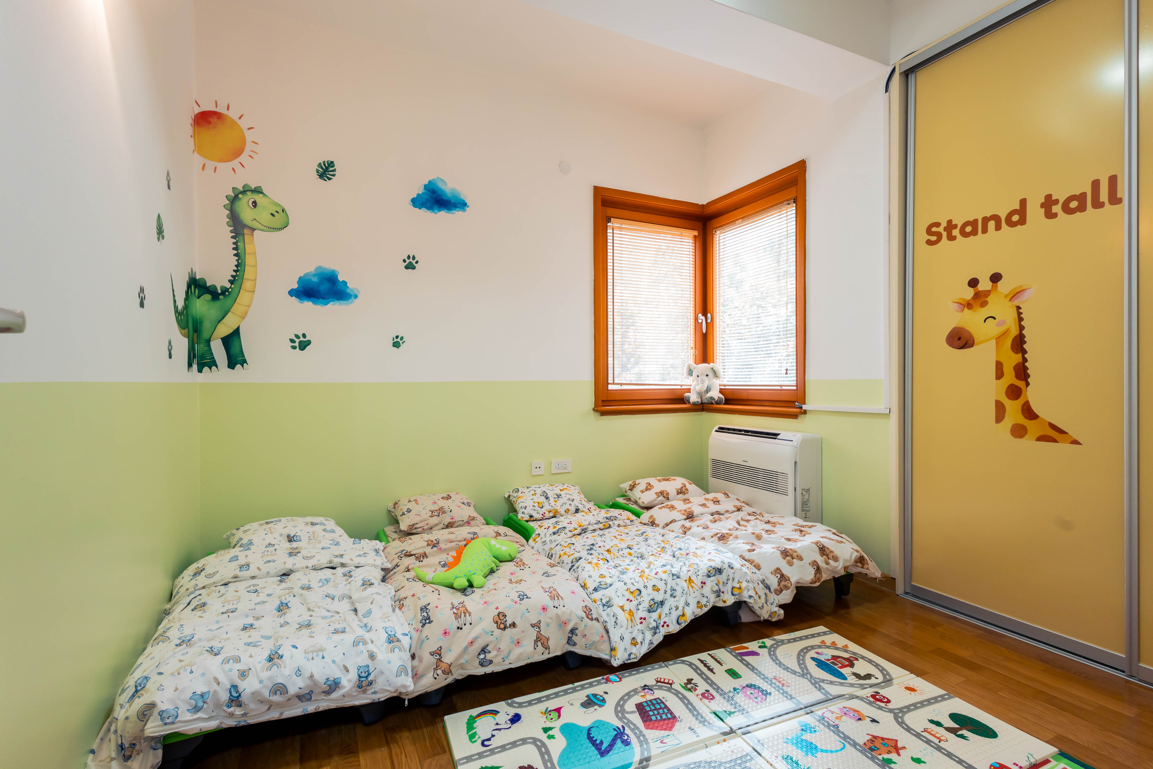 Cozy nap room with soft floor beds and a friendly dinosaur mural